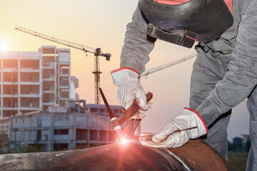 Construction Worker welder process structure at site project with spark light and wear equipment protective, PPE and building with crane construction background.