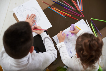 Top view of two children drawing with color pencils at home