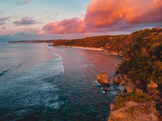 Aerial view of rocky coastline with cliff, ocean and bright clouds at warm sunset