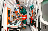 Fototapeta  - A male paramedic in uniform puts on a ventilator with oxygen to help a senior patient lying on a gurney with a pulse oximeter in a modern ambulance.