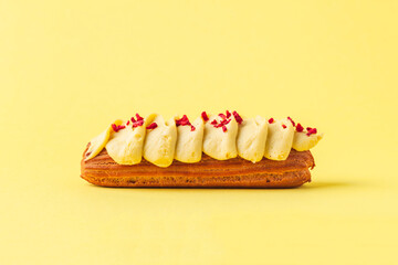 Wall Mural - Fresh eclair with  butter cream filling and original decoration. French pastry on the yellow background. Macro shot