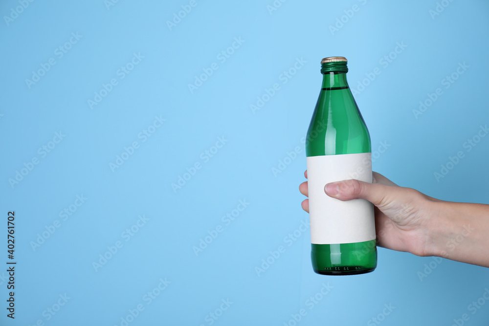 Woman holding glass bottle with soda water on light blue background, closeup. Space for text - obrazy, fototapety, plakaty 
