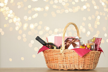 Wicker basket with gifts, wine and food against blurred festive lights. Space for text