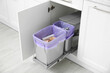 © New Africa - Open cabinet with full trash bins for separate waste collection in kitchen
