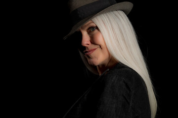 Wall Mural - Image of a beautiful mature woman with platinum blonde hair, wearing a hat. Studio image with a black background.