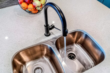 Water From Black Curved Faucet Running Down Stainless Steel Sink With Two Bowls