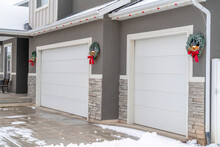 White Garage Doors Of Home With Festive Wreaths Mounted On The Gray Wall