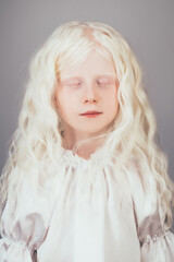 Wall Mural - Sweet little girl. Angel innocence. Child dream. Portrait of adorable cute peaceful albino blonde kid with white curly hair eyebrows closed eyes in vintage blouse isolated on gray background.