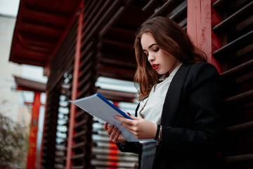 Wall Mural - Young woman ginger redhead girl hold folder with documents. Pretty serious confident lady, daily distance remote work. Small business owner standing outside, dressed blazer with white shirt.