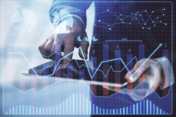 Double exposure of man's hands holding and using a digital device and forex graph drawing. Financial market concept.