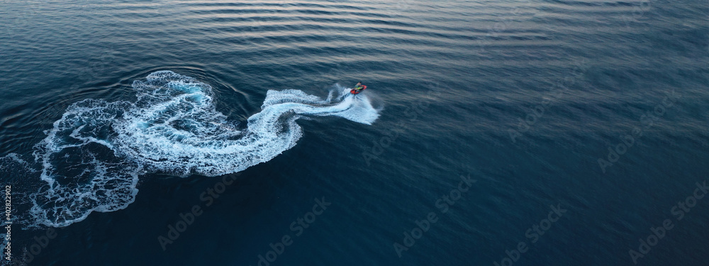 Aerial drone ultra wide photo of jet ski watercraft performing extreme manoeuvres in deep blue bay with calm sea at dusk - obrazy, fototapety, plakaty 