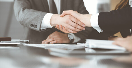 Unknown businessman shaking hands with his colleague or partner above the glass desk in modern office, close-up. Business people group at meeting