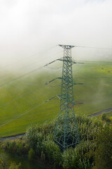 Aerial view of the high voltage power lines and high voltage electric transmission on the terrain in clouds surrounded by trees at sunlight