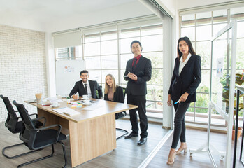 Wall Mural - Portrait of young and successful caucasian and asian co-workers in suit wear meeting and look at camera while standing in working space