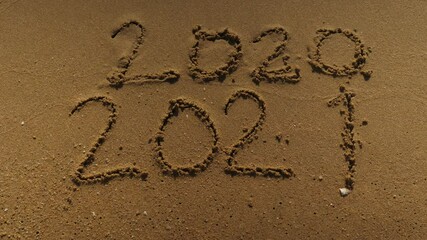 Wall Mural - Message Year 2020 replaced by 2021 written on beach sand background. Good bye 2020 hello to 2021 Lapping waves happy New Year coming concept
