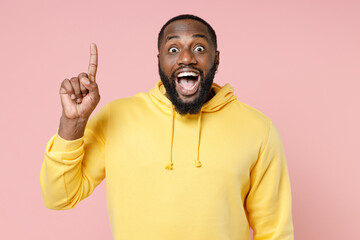 Wall Mural - Excited young african american man 20s wearing casual basic yellow streetwear hoodie standing holding hands folded in prayer looking camera isolated on pastel pink color background studio portrait.