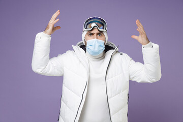 Wall Mural - Irritated skier man in white windbreaker jacket ski goggles face mask to safe from coronavirus virus covid-19 spreading hands weekend in mountains isolated on purple background. People hobby concept.