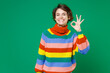 © ViDi Studio - Smiling cheerful beautiful funny young brunette woman 20s years old in basic colorful sweater standing showing ok okay gesture looking camera isolated on bright green color background studio portrait.
