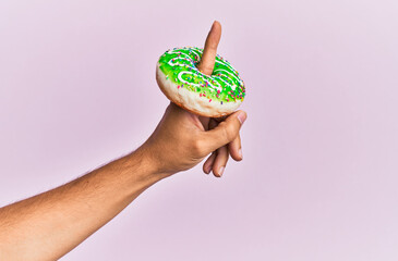 Wall Mural - Finger of hispanic man holding donut over isolated pink background.