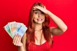 Young beautiful redhead woman holding south korean won banknotes stressed and frustrated with hand on head, surprised and angry face