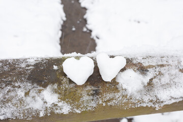 two white hearts made of snowballs on wooden railing, forest landscape background, river