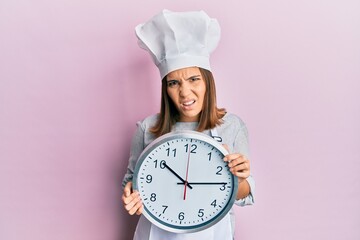 Sticker - Young beautiful woman wearing professional cook uniform and hat holding clock clueless and confused expression. doubt concept.