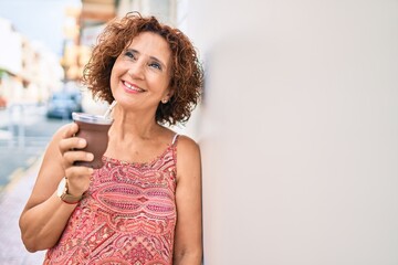 Poster - Middle age woman smiling happy leaning on the wall at street of city.