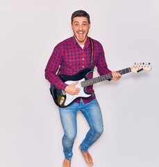 Wall Mural - Young handsome hispanic artist man playing electric guitar. Jumping with open mouth over isolated white background