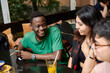 © etonastenka - A young black man telling a joke to his girlfriend surrounded by friends in a modern coffee shop