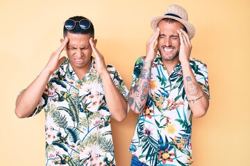 Young gay couple of two men wearing summer hat and hawaiian shirt with hand on head, headache because stress. suffering migraine.