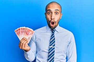 Canvas Print - Hispanic adult man holding 20 israel shekels banknotes scared and amazed with open mouth for surprise, disbelief face