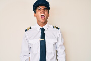 Sticker - Young hispanic man wearing airplane pilot uniform angry and mad screaming frustrated and furious, shouting with anger. rage and aggressive concept.