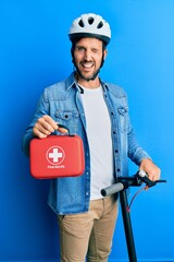 Wall Mural - Young man standing on scooter wearing helmet holding first aid kit winking looking at the camera with sexy expression, cheerful and happy face.