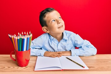 Wall Mural - Adorable caucasian kid writing book sitting on the table looking to side, relax profile pose with natural face and confident smile.