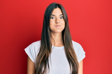 Sticker - Young brunette woman wearing casual white tshirt over red background puffing cheeks with funny face. mouth inflated with air, crazy expression.