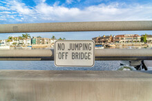 No Jumping Off Bridge Sign With Sea Waterfront Houses And Cloudy Sky Background