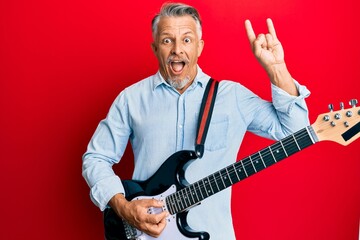 Wall Mural - Middle age grey-haired man playing electric guitar doing rock sign celebrating crazy and amazed for success with open eyes screaming excited.