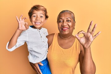 Hispanic grandson and grandmother together over yellow background doing ok sign with fingers, smiling friendly gesturing excellent symbol