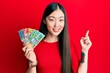 © Krakenimages.com - Young chinese woman holding australian dollars smiling happy pointing with hand and finger to the side