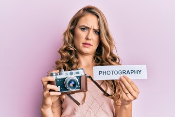 Sticker - Young blonde girl holding vintage camera and paper with photography word paper clueless and confused expression. doubt concept.