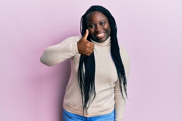 Poster - Young black woman with braids wearing casual winter sweater doing happy thumbs up gesture with hand. approving expression looking at the camera showing success.