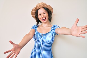 Young beautiful girl wearing summer hat looking at the camera smiling with open arms for hug. cheerful expression embracing happiness.