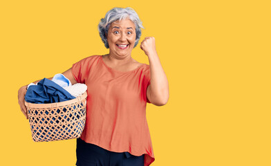 Poster - Senior woman with gray hair holding laundry basket screaming proud, celebrating victory and success very excited with raised arms