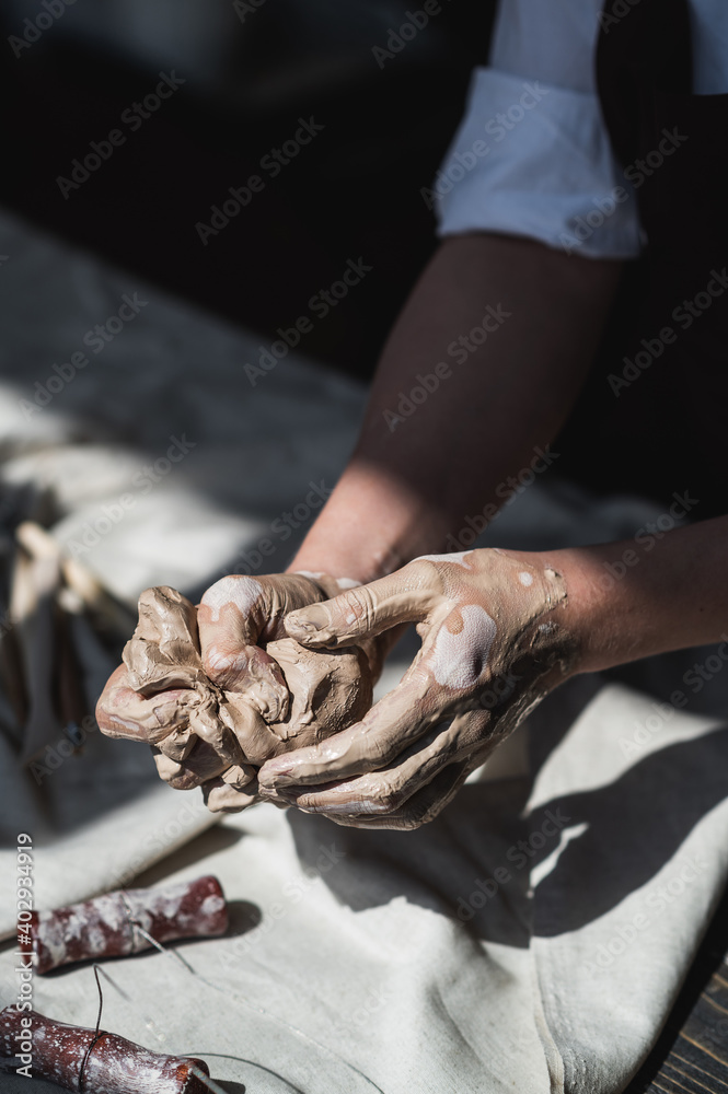 Woman's hands wet and dirty after working with clay in a pottery studio - obrazy, fototapety, plakaty 