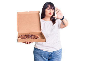 Sticker - Young plus size woman holding delivery pizza box with open hand doing stop sign with serious and confident expression, defense gesture