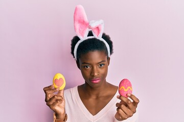 Canvas Print - Young african american girl wearing cute easter bunny ears holding painted eggs relaxed with serious expression on face. simple and natural looking at the camera.