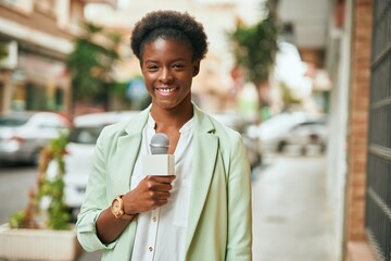 Canvas Print - Young african american reporter woman using microphone at the city