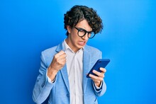 Hispanic Young Man Using Smartphone Wearing Business Jacket Annoyed And Frustrated Shouting With Anger, Yelling Crazy With Anger And Hand Raised