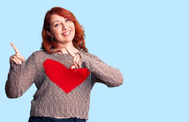 Poster - Young beautiful redhead woman wearing casual heart sweater smiling and looking at the camera pointing with two hands and fingers to the side.