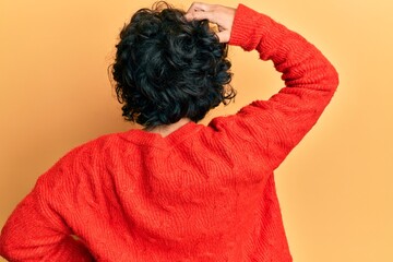 Young hispanic woman with curly hair wearing casual winter sweater backwards thinking about doubt with hand on head